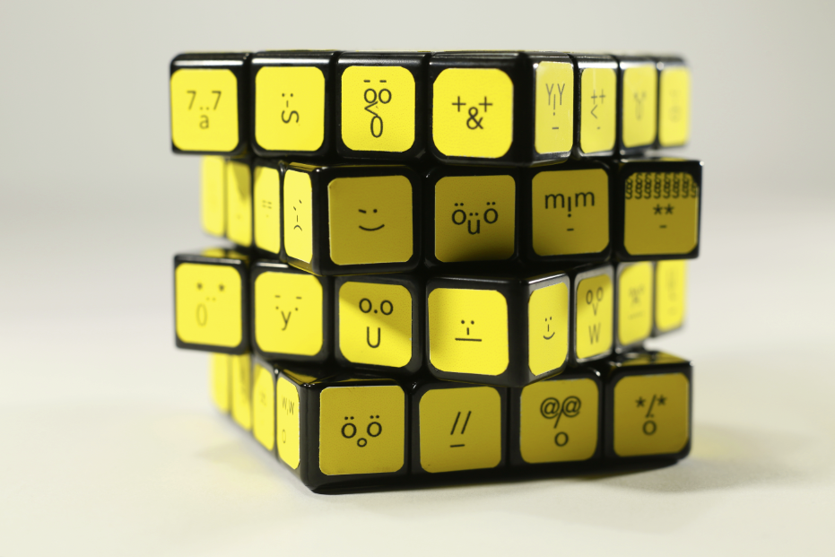 A still image of a yellow Rubik's cube. The small cubes are collaged with smileys. Each cube has a different smiley.